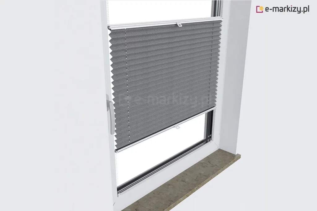 Zdjęcie wykonane z perspektywy bocznej, pod kątem, prezentujące białe okno z PCV z zamontowaną szarą plisą okienną. Plisa okienna jest ustawiona w pozycji środkowej, zasłaniając centralną część szyby, podczas gdy górny i dolny fragment okna pozostają odsłonięte. Materiał osłony ma głęboki, grafitowy odcień i regularną strukturę poziomych zakładek tworzących efekt harmonijki. Tkanina jest rozpięta na białych, aluminiowych profilach ruchomych, które przesuwają się wzdłuż bocznych listew przyoszybowych dzięki systemowi cienkich, białych sznurków prowadzących widocznych na powierzchni materiału. Na obu profilach sterujących zamontowane są centralne uchwyty z tworzywa sztucznego. Okno posiada klasyczną białą klamkę po lewej stronie ramy. W dolnej części kadru widoczny jest fragment kamiennego parapetu o matowej, ziarnistej strukturze w kolorze beżowo-szarym. Całość kompozycji na tle czystej, białej ściany podkreśla nowoczesny design i funkcjonalność plisy okiennej, pozwalającej na precyzyjne zarządzanie dopływem światła przy zachowaniu estetycznego wyglądu wnęki okiennej.