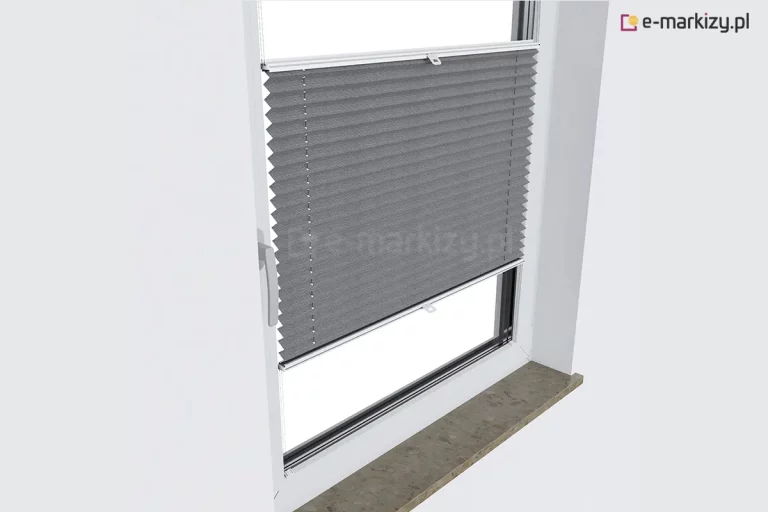 Zdjęcie wykonane z perspektywy bocznej, pod kątem, prezentujące białe okno z PCV z zamontowaną szarą plisą okienną. Plisa okienna jest ustawiona w pozycji środkowej, zasłaniając centralną część szyby, podczas gdy górny i dolny fragment okna pozostają odsłonięte. Materiał osłony ma głęboki, grafitowy odcień i regularną strukturę poziomych zakładek tworzących efekt harmonijki. Tkanina jest rozpięta na białych, aluminiowych profilach ruchomych, które przesuwają się wzdłuż bocznych listew przyoszybowych dzięki systemowi cienkich, białych sznurków prowadzących widocznych na powierzchni materiału. Na obu profilach sterujących zamontowane są centralne uchwyty z tworzywa sztucznego. Okno posiada klasyczną białą klamkę po lewej stronie ramy. W dolnej części kadru widoczny jest fragment kamiennego parapetu o matowej, ziarnistej strukturze w kolorze beżowo-szarym. Całość kompozycji na tle czystej, białej ściany podkreśla nowoczesny design i funkcjonalność plisy okiennej, pozwalającej na precyzyjne zarządzanie dopływem światła przy zachowaniu estetycznego wyglądu wnęki okiennej.