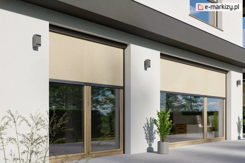 Fragment parterowej części elewacji budynku w stylu modernistycznym z dużymi przeszkleniami tarasowymi, zasłoniętymi zewnętrznymi osłonami Refleksol 90 Selt. System screenowy zastosowany na zdjęciu wyposażony jest w prowadnice boczne i estetyczne, zaokrąglone kasety, które harmonijnie łączą się z bryłą budynku. Jasnobeżowa tkanina screenowa, o drobno tkanej strukturze, częściowo zacienia okna, tworząc delikatny cień wewnątrz pomieszczeń. Dolna część szyb pozostaje odkryta, umożliwiając widok na zewnątrz – widać przez nie nowoczesne, drewniane meble oraz zieloną roślinność w ogrodzie. Elewacja utrzymana w jasnych kolorach kontrastuje z ciemnymi akcentami kaset i obramowań okiennych, a całość kompozycji podkreśla funkcjonalny i jednocześnie estetyczny charakter zastosowanych rozwiązań przeciwsłonecznych. Rośliny doniczkowe i cień rzucony przez liście na elewację dodają naturalnego charakteru przestrzeni tarasowej.