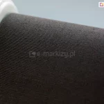 Zbliżenie tkaniny roletowej w kolorze brązowym oraz lewego mocowania rolety PLUS w kolorze białym.