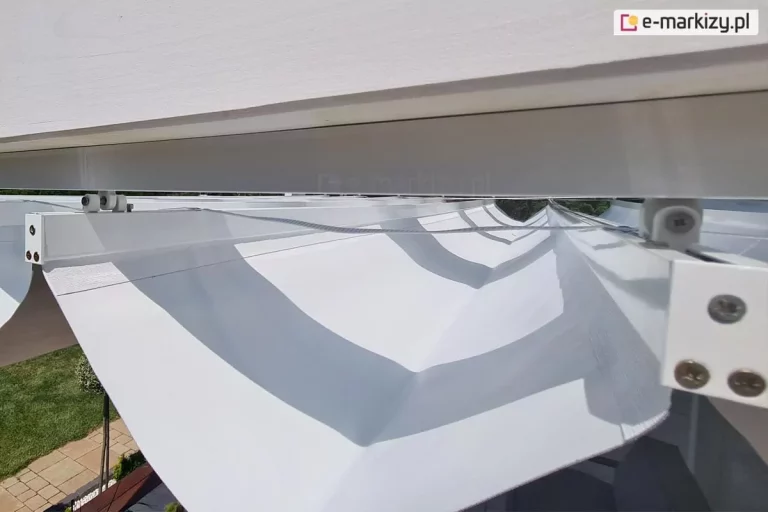 Zbliżenie na mocowanie opcjonalnego dachu rzymskiego Supro do konstrukcji pergoli drewnianej Moza, wszystkie elementy wykonane w kolorze białym.