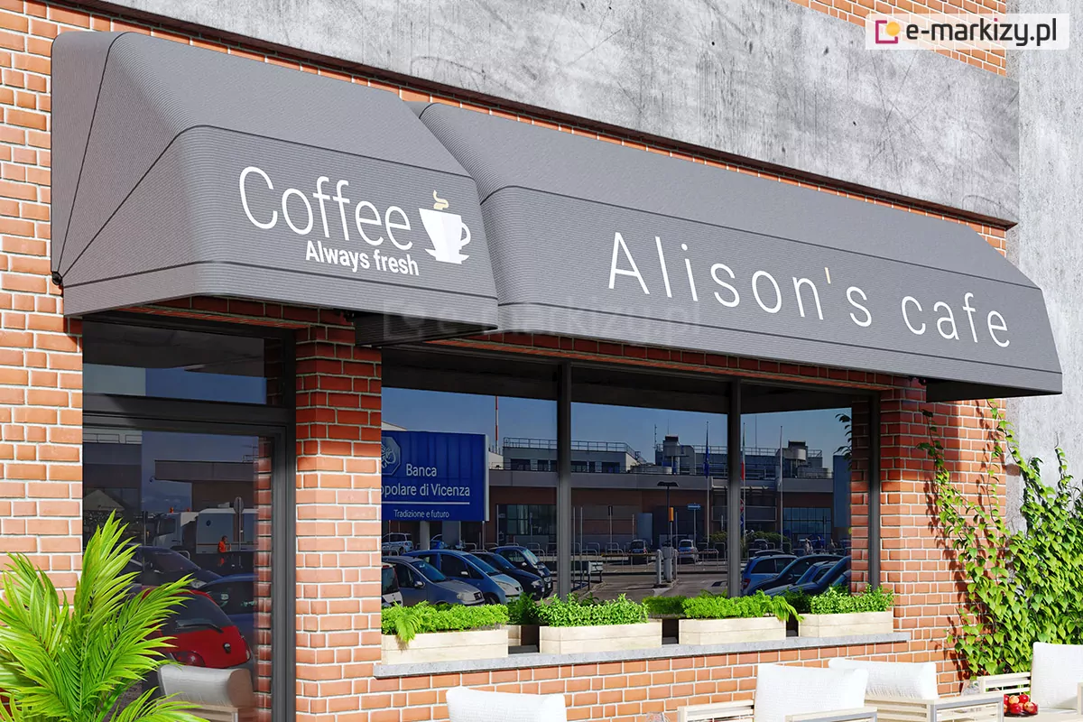 Zdjęcie przedstawia elewację kawiarni wykonaną z jasnoczerwonej cegły, na której zamontowano dwie grafitowe markizy koszowe o nowoczesnym, prostokątnym profilu. Markizy reklamowe są zamontowane modułowo: mniejsza osłona znajduje się nad drzwiami wejściowymi i posiada biały napis „Coffee Always fresh” wraz z grafiką filiżanki, natomiast szersza markiza osłania dużą witrynę okienną i widnieje na niej napis „Alison's cafe”. Poszycie markiz jest jednolite, o matowej teksturze, z wyraźnie zaznaczonymi krawędziami stelaża. Pod markizami, na parapecie witryny, ustawiono podłużne jasne donice z gęstą, zieloną roślinnością. W szybach witryny odbija się fragment miejskiej infrastruktury, parking oraz niebieski szyld informacyjny. Po lewej stronie kadru widoczny jest fragment egzotycznej rośliny doniczkowej, a po prawej pnącze wspinające się po ceglanej ścianie, co nadaje wejściu do lokalu przytulny charakter.