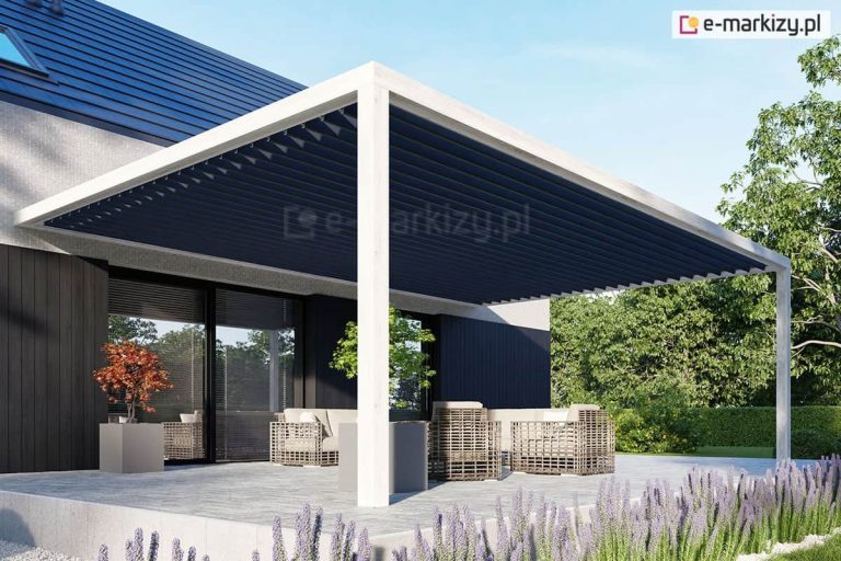 Nowoczesny taras z zabudową przyścienną, tworzącą zadaszenie nad powierzchnią tarasu. Konstrukcja pergoli przyściennej wsparta jest na dwóch białych, smukłych słupach o kwadratowym przekroju, które podtrzymują ramę o tym samym kolorze. Zadaszenie pergoli stanowi dach lamelowy SB400 MD, który składa się z gęsto rozmieszczonych lameli w kolorze antracytowym. Lamele całkowicie zamknięte, tworząc jednolitą, ciemną płaszczyznę chroniącą przed słońcem i deszczem. Pod pergolą znajduje się strefa wypoczynkowa z jasnymi, plecionymi meblami ogrodowymi i szarymi poduszkami. Taras został wyłożony wielkoformatowymi płytami w kolorze jasnoszarym, a wzdłuż jego krawędzi posadzono ozdobną lawendę. Budynek posiada nowoczesną elewację łączącą biały tynk z ciemnym deskowaniem oraz duże przeszklenia z widocznymi żaluzjami fasadowymi. Całość kompozycji dopełnia soczysta zieleń ogrodu i drzewa liściaste w tle pod bezchmurnym, błękitnym niebem.