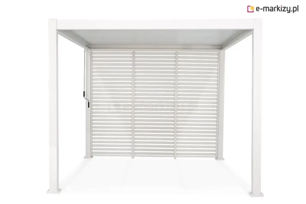 Biała pergola ogrodowa Gloria z pełną zabudową tylnej ściany wykonaną z trzech stałych paneli żaluzjowych. Panele są zamontowane obok siebie, wypełniając całkowicie przestrzeń między dwoma tylnymi słupami konstrukcji. Każdy moduł składa się z poziomych, równolegle ułożonych lameli aluminiowych w kolorze białym, które tworzą spójną barierę wizualną, przepuszczając jednocześnie powietrze. Cała konstrukcja, włączając cztery pionowe słupy z kwadratowymi podstawami oraz ramy paneli, jest wykończona w jednolitym białym kolorze. Po lewej stronie, przy przednim słupie, widoczny jest pionowy drążek mechanizmu korbowego do regulacji zadaszenia. Wnętrze pergoli jest puste, a podłoże oraz tło są jasne i jednolite.