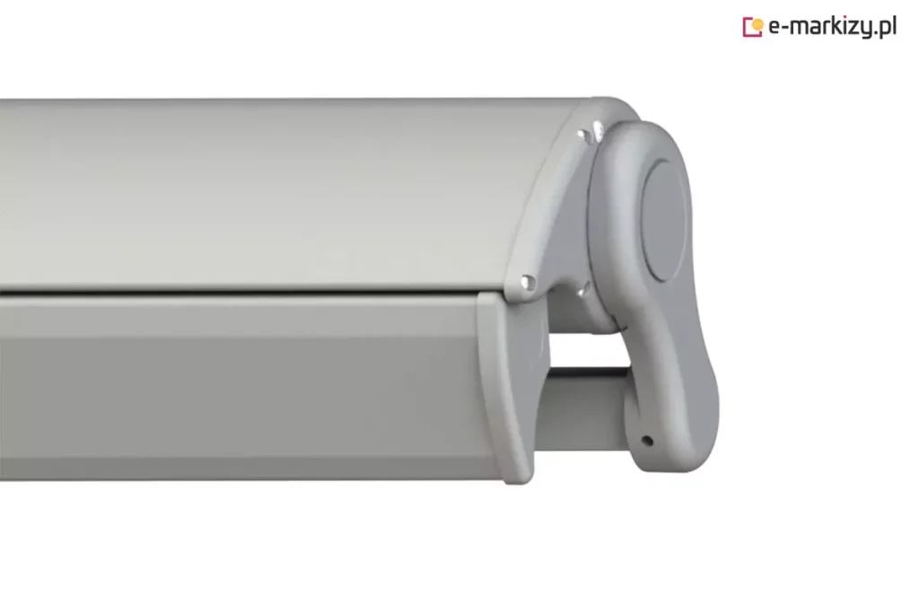 Zdjęcie prezentuje zbliżenie na system domykania, który posiada markiza Tremolo, ukazany w rzucie bocznym na białym tle. Aluminiowa konstrukcja w kolorze szarym składa się z profilu górnego kasety oraz idealnie dopasowanej belki frontowej, która w pozycji złożonej tworzy szczelną osłonę dla mechanizmu i tkaniny. Widoczna jest boczna pokrywa o obłym kształcie, przymocowana za pomocą estetycznych śrub, oraz fragment ramienia chowającego się wewnątrz obudowy. Precyzyjne spasowanie elementów profilu bocznego podkreśla nowoczesny design produktu oraz funkcję ochronną pełnej kasety, która zabezpiecza komponenty przed niekorzystnymi warunkami pogodowymi.