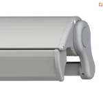 Zdjęcie prezentuje zbliżenie na system domykania, który posiada markiza Tremolo, ukazany w rzucie bocznym na białym tle. Aluminiowa konstrukcja w kolorze szarym składa się z profilu górnego kasety oraz idealnie dopasowanej belki frontowej, która w pozycji złożonej tworzy szczelną osłonę dla mechanizmu i tkaniny. Widoczna jest boczna pokrywa o obłym kształcie, przymocowana za pomocą estetycznych śrub, oraz fragment ramienia chowającego się wewnątrz obudowy. Precyzyjne spasowanie elementów profilu bocznego podkreśla nowoczesny design produktu oraz funkcję ochronną pełnej kasety, która zabezpiecza komponenty przed niekorzystnymi warunkami pogodowymi.