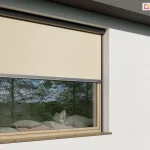 Nowoczesna fasada budynku mieszkalnego zbliżoną do stylu minimalistycznego, gdzie główną rolę pełni osłona okienna Refleksol 90 Selt z prowadnicami bocznymi. Tkanina screenowa w kolorze ciepłego beżu została częściowo opuszczona, zasłaniając górną część przeszklenia, co chroni wnętrze przed bezpośrednim nasłonecznieniem, a jednocześnie pozostawia dolną część szyby odkrytą. Dzięki temu uzyskano optymalny balans pomiędzy światłem dziennym a ochroną termiczną. Przez szybę widoczne jest przytulne wnętrze z szerokim parapetem pełniącym funkcję siedziska – z miękkimi poduszkami w pastelowych kolorach i tkaninach dekoracyjnych. Refleksol zamocowany jest w delikatnej, zaokrąglonej kasecie w kolorze antracytowym, tak, jak prowadnice, co podkreśla nowoczesny charakter okna. Tkanina ma subtelną, siatkową strukturę, która przepuszcza światło i pozwala na kontakt wzrokowy z otoczeniem przy zachowaniu prywatności.