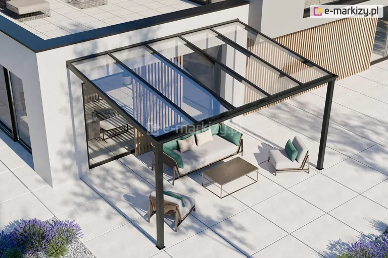 nowoczesne zadaszenie tarasowe model Terano, zamontowane do białej elewacji piętrowego budynku o minimalistycznej architekturze. Konstrukcja wykonana jest z profili aluminiowych w kolorze czarnym lub antracytowym i składa się z dwóch pionowych słupów wspierających oraz ramy dachowej wypełnionej pięcioma taflami przezroczystego szkła. Dach posiada lekki spadek, co umożliwia swobodny odpływ wody opadowej. Pod zadaszeniem zaaranżowano strefę wypoczynkową z nowoczesnymi meblami ogrodowymi: szarą sofą z zielonymi poduszkami, dwoma fotelami w tym samym stylu oraz niskim prostokątnym stolikiem kawowym o ciemnym blacie. Podłoże tarasu wyłożone jest dużymi, jasnymi płytami betonowymi lub ceramicznymi o kwadratowym kształcie. W tle widoczne są duże przeszklenia drzwi tarasowych oraz pionowe lamele dekoracyjne wykonane z jasnego drewna, zamontowane na ścianie budynku. W dolnym lewym rogu kadru widać fragmenty ozdobnej roślinności w postaci kęp lawendy posadzonej w białym żwirze. Całość kompozycji jest oświetlona jasnym, dziennym światłem, rzucającym wyraźne cienie konstrukcji na powierzchnię tarasu.