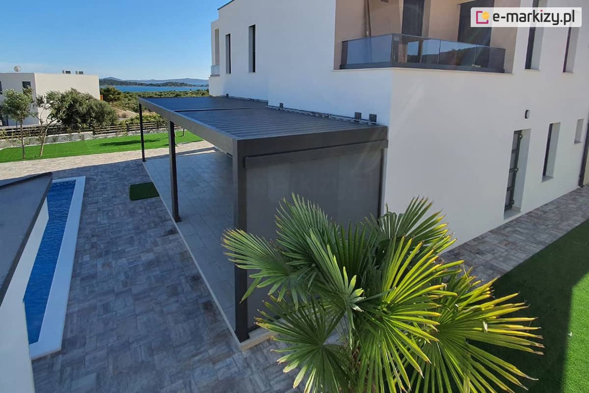 Pergola przyścienna z lamelami ustawionymi prostopadle do ściany, dzięki dwóm modułom uzyskano spójne zadaszenie dla tarasu o nietypowym kształcie