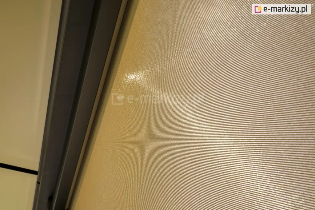 Zbliżenie tkaniny refleksola w kolorze kremowym, która przepuszcza około 5{e3933235a64fccd7de26a4f842e7e798e8da8f3cc380da0bec2b0bf1a35f755f} promieniowania słonecznego, zapewniając jednocześnie cień i ochronę przed słońcem oraz odpowiednią ilość światła.