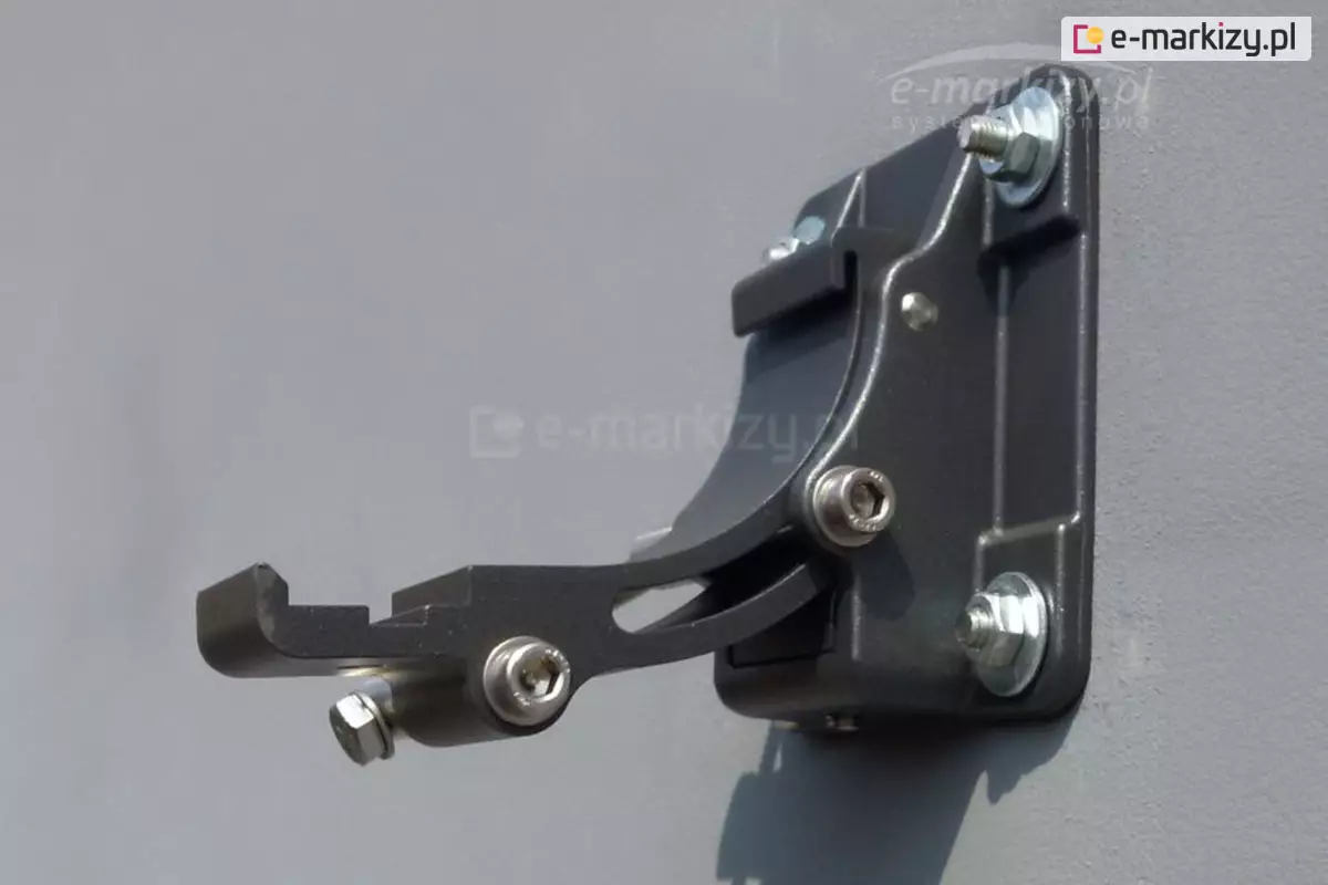 Zamocowany do ściany pomalowanej na szaro konsolowy uchwyt ścienny do markizy Dakar i Casablanca w kolorze srebrzysty grafit. Mocowanie uchwytu do ściany za pomocą czterech śrub. W wystającej części uchwytu widoczne zagłębienie, w którym powinien się znaleźć rowek w dolnej części kasety markizy.