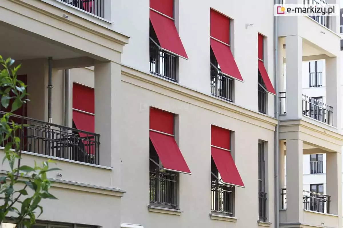 Wielopiętrowy duży budynek, w którym wiele okien osłoniętych zostało markizoletą 120 podtynkową z czerwoną tkaniną.