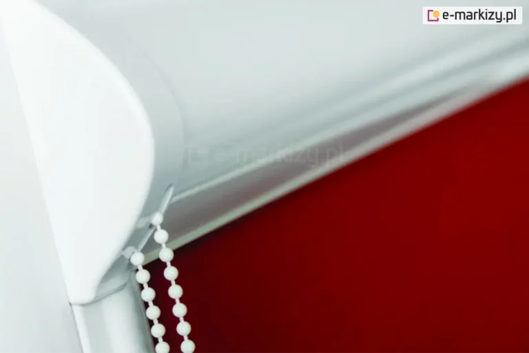 Biała kasetka rolety materiałowej na okno z ukrytym w niej mechanizmem łańcuszkowego sterowania osłoną wtapia się w kolor ramy okna, a czerwona tkanina nadaje całości wyrazistego charakteru.