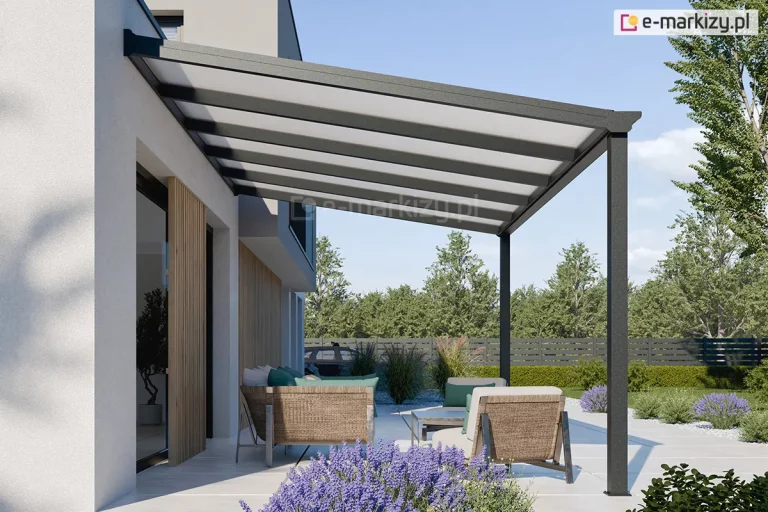 Nowoczesna wiata tarasowa Lunaro w kolorze antracytowym, zamontowana do jasnej elewacji nowoczesnego domu. Jednospadowy dach konstrukcji wypełniają panele z poliwęglanu komorowego w kolorze mlecznym, które opierają się na systemowych, ciemnych krokwiach. Pod zadaszeniem, na tarasie wyłożonym białymi płytami, znajduje się strefa wypoczynkowa z wygodnymi, beżowymi fotelami i sofą ozdobioną turkusowymi poduszkami. Aranżację dopełniają lawendowe kępy kwiatów na pierwszym planie oraz widok na ogród z zielonymi drzewami i niskim żywopłotem pod czystym niebem.