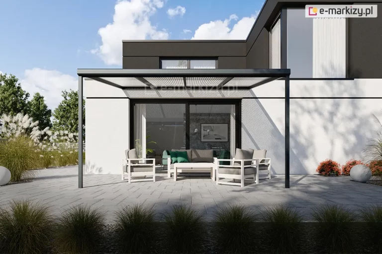 Zdjęcie prezentuje wizualizację nowoczesnego tarasu przy budynku o minimalistycznej architekturze, osłoniętego zadaszeniem Nebbiolo marki Deponti. Konstrukcja zadaszenia opiera się na antracytowym, aluminiowym stelażu z dachem wypełnionym transparentnym poliwęglanem komorowym, który rzuca liniowy cień na jasną elewację domu. Pod zadaszeniem ustawiono komplet nowoczesnych mebli ogrodowych w kolorze białym z szarymi poduszkami, składający się z sofy, dwóch foteli oraz niskiego stolika kawowego. Szerokie, przeszkolone drzwi przesuwne prowadzą z tarasu bezpośrednio do wnętrza salonu. Nawierzchnia tarasu wykonana jest z dużych, jasnoszarych płyt betonowych, a w jego otoczeniu znajdują się ozdobne trawy w donicach oraz niska roślinność ogrodowa. Całość kompozycji utrzymana jest w chłodnej, nowoczesnej stylistyce pod jasnym niebem z delikatnymi chmurami.