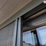 Moskitiera plisowana Top Zag zamontowana we wnęce okiennej tuż przy ramie oknie o antracytowym kolorze, pakiet z plisowaną siatką przesuwa się wewnątrz profilu górnego, co zapewnia jeszcze lepszą ochronę przed owadami.