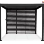 Wolnostojąca pergola tarasowa Gloria w kolorze ciemnografitowym zaprezentowana na białym tle w ujęciu od frontu ukazującym jej geometryczną konstrukcję oraz system osłon bocznych. Konstrukcja wspiera się na czterech solidnych aluminiowych słupach o kwadratowym przekroju, które zwieńczone są płaskim dachem o prostej linii. Tylna ściana pergoli została niemal w całości wypełniona trzema szerokimi panelami przesuwnymi z poziomymi lamelami, które tworzą estetyczną żaluzję zapewniającą prywatność oraz ochronę przed słońcem przy jednoczesnym zachowaniu cyrkulacji powietrza. Po lewej stronie konstrukcji, przy słupie, widoczny jest pionowy mechanizm korbowy służący do ręcznej regulacji ustawienia zadaszenia lub ścianek. Całość konstrukcji malowana jest proszkowo na matowy, bardzo ciemny odcień szarości, co nadaje produktowi nowoczesny i minimalistyczny charakter pasujący do współczesnej architektury ogrodowej. Detale wykończenia, takie jak stopy montażowe przy podstawie słupów, sugerują stabilny montaż do podłoża, a precyzyjne łączenia elementów podkreślają wysoką jakość wykonania aluminiowej altany.