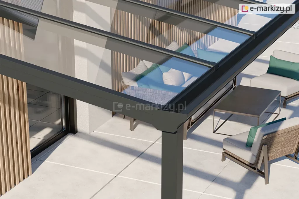 Zadaszenie tarasu ze szkła Terano z klasycznym wykończeniem belki przedniej, w której ukryta jest rynna. Pod antracytową konstrukcją zadaszenia oraz przejrzystym szkłem widoczny taras wyłożony dużymi jasnymi płytkami oraz zestaw mebli z rattanu z poduchami w kolorach szarym i zielonym, a także niski stolik kawowy w odcieniu grafitowym.