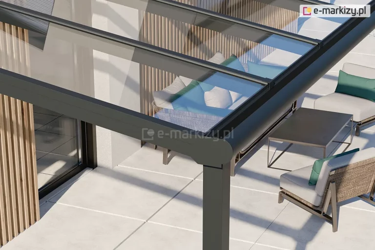 Zbliżenie na górną konstrukcję nowoczesnego zadaszenia aluminiowego Terano, wykonanego w stylu nowoczesnym, z zaokrągloną rynną. Na pierwszym planie widoczny jest pionowy słup nośny o przekroju kwadratowym, połączony z rynną o charakterystycznym, zaokrąglonym profilu frontowym. Konstrukcja została wykonana z profili aluminiowych w kolorze antracytowym o matowej powierzchni. Dach zadaszenia jest w całości przeszklony, a szklane panele są osadzone w systemie krokwi aluminiowych, co zapewnia pełną przezierność. Pod zadaszeniem widoczna jest strefa wypoczynkowa zaaranżowana na jasnoszarych, wielkoformatowych płytach tarasowych. Wyposażenie obejmuje nowoczesne fotele z jasnymi poduchami i turkusowymi akcentami oraz minimalistyczny, prostokątny stolik z ciemnym blatem. W tle widoczna jest biała elewacja budynku z dekoracyjnymi, pionowymi lamelami drewnianymi oraz duże przeszklenia drzwi tarasowych. Całość kompozycji ukazana w świetle dziennym podkreśla technologiczną precyzję wykonania i nowoczesny design zabudowy.