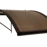 Daszek nad drzwi jednostronnie łukowy w kolorze brązowym z wypełnieniem z poliwęglanu dymionego zakrzywiony na prawy bok, zamocowany do białej ściany.