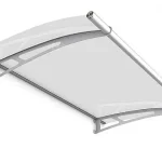 Produktowa wizualizacja przedstawia nowoczesne zadaszenie drzwiowe o łukowej konstrukcji, zamontowane na jasnym tle. Głównym elementem jest półprzezroczysta płyta akrylowa wypełniająca o matowym, satynowym wykończeniu, która łagodnie rozprasza światło. Całość opiera się na dwóch symetrycznie rozmieszczonych wspornikach bocznych wykonanych z metalu w kolorze srebrnym lub satynowym chromie. Wsporniki mają charakterystyczną, ażurową konstrukcję z trójkątnymi wycięciami, co nadaje im wizualnej lekkości przy zachowaniu stabilności. Górna krawędź daszka, przylegająca do ściany, oraz krawędź przednia są wykończone profilami maskującymi. Na przedniej krawędzi widoczna jest zintegrowana rynienka odpływowa o okrągłym przekroju, zakończona estetycznymi zaślepkami po bokach. Konstrukcja jest nachylona pod kątem, co ułatwia swobodny odpływ wody deszczowej oraz zsuwanie się śniegu.