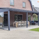 Zadaszenie ze szkła nad dużym tarasem z częścią wypoczynkową oraz dużym stołem