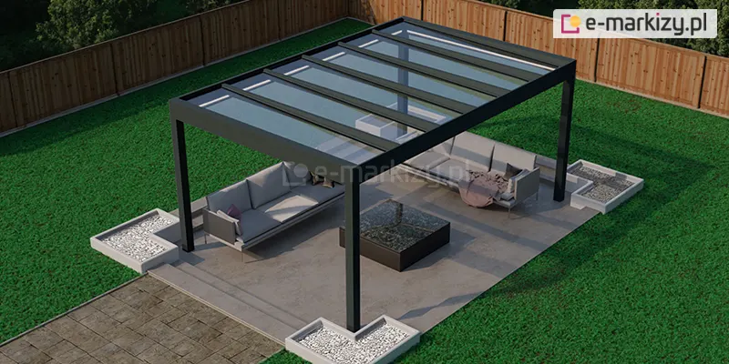 Nowoczesna, wolnostojąca konstrukcja zadaszenia tarasowego o nazwie Pinela Glass marki Deponti, Spekta Glas, usytuowana w ogrodzie na planie prostokąta. Konstrukcja nośna została wykonana z grubych profili aluminiowych w kolorze antracytowym, które tworzą minimalistyczną ramę z czterema pionowymi słupami wspierającymi dach. Dach konstrukcji jest w całości przeszklony i podzielony na sześć szerokich, poprzecznych paneli szklanych, co zapewnia pełną przezierność i maksymalne doświetlenie strefy wypoczynku. Pod zadaszeniem zaaranżowano nowoczesny salon ogrodowy na betonowym fundamencie wykonanym z dużych, jasnoszarych płyt tarasowych. Wewnątrz znajdują się dwie narożne sofy z jasnoszarymi poduszkami oraz centralnie ustawiony kwadratowy stolik kawowy z ciemnym, błyszczącym blatem. Wokół stóp konstrukcji umieszczono geometryczne, betonowe donice w formie kwadratowych ram wypełnionych białym gresem, które wyznaczają granice tarasu. Całość otacza intensywnie zielony, zadbany trawnik, a w tle widoczne jest wysokie, drewniane ogrodzenie z pionowych paneli, które zapewnia prywatność posesji.