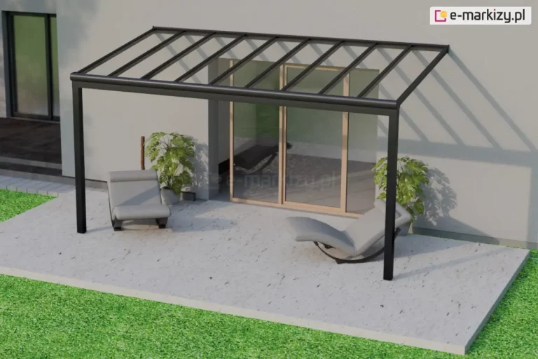 Elegancki, minimalistyczny taras z prostym zadaszeniem wykonanym z przezroczystego poliwęglanu osadzonego na ciemnej, aluminiowej ramie. Konstrukcja wsparta jest na dwóch słupach frontowych i przytwierdzona do ściany domu, której powierzchnia jest jasna i gładka. Cień konstrukcji dachowej tworzy na elewacji wyraźny wzór ukośnych linii. Na tarasie znajdują się dwa leżaki – szare, nowoczesne, z ergonomicznym kształtem i czarną, półokrągłą podstawą umożliwiającą bujanie. Leżak po lewej stronie ustawiony jest frontem do aparatu, natomiast prawy bokiem. Obok obu mebli stoją duże donice z zielonymi roślinami ozdobnymi. Za leżakami, centralnie w tle, znajdują się przesuwne drzwi tarasowe z ramą w kolorze jasnego drewna. W odbiciu szyby w drzwiach tarasowych widoczny jest jeszcze jeden leżak, częściowo schowany w cieniu. Na lewym krańcu kadru widać fragment bocznej części budynku, z dużym, przyciemnianym oknem oraz stopniem prowadzącym na wyłożoną płytkami powierzchnię. Przestrzeń tarasowa pokryta jest jasną, marmurkową posadzką i otoczona pasem żywozielonej trawy.