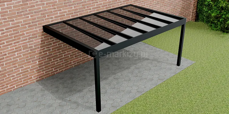 Szklane zadaszenie tarasu Spekta Glass przymocowane do ściany budynku z czerwonej cegły. Czarna konstrukcja i przejrzyste szkło zamocowane zostały nad tarasem z szarej kostki brukowej w pobliżu sporego trawnika pozbawionego ozdób.