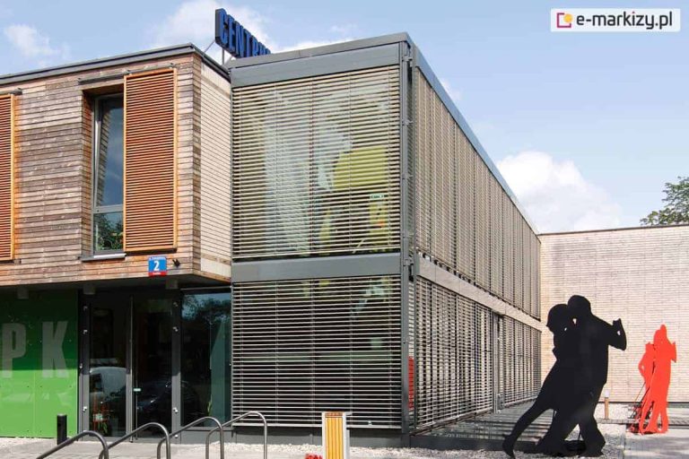 Żaluzje fasadowe Z90 Oval jako osłona pojedyncza i modułowa na budynku dużego biurowca, przed którym ustawiono kartonowe wizerunki tancerzy