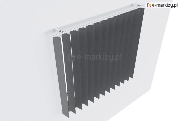 Zdjęcie przedstawia widok z góry na żaluzje pionowe vertikal zamontowane na ścianie nad oknem za pomocą specjalnych białych wsporników dystansowych. Ciemnoszare, antracytowe lamele wykonane z gęstej tkaniny o delikatnej strukturze są ustawione pod kątem, tworząc rytmiczny szereg pionowych pasów. Szyna montażowa jest koloru białego i została przytwierdzona do gładkiej, jasnej ściany, wystając poza jej płaszczyznę, aby zapewnić swobodną pracę materiału. Wąskie pasy tkaniny zwisają swobodnie, a w dolnej części połączone są dyskretnym, białym łańcuszkiem kulkowym, który stabilizuje żaluzje pionowe vertikal i zapobiega ich plątaniu. Perspektywa z ukosu ukazuje techniczny aspekt montażu oraz sposób, w jaki osłona przesłania wnękę okienną, oferując nowoczesny wygląd i funkcjonalność w regulacji światła.