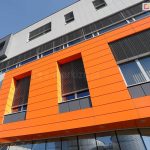 Przykład wykorzystania żaluzji fasadowych podtynkowych do osłony wielu okien w nowoczesnej fasadzie. Ukryte pod warstwą tynku o szarym i pomarańczowym kolorze skrzynki nie zakłócają geometrii elewacji, a jednocześnie chronią pomieszczenia przed nagrzewaniem.