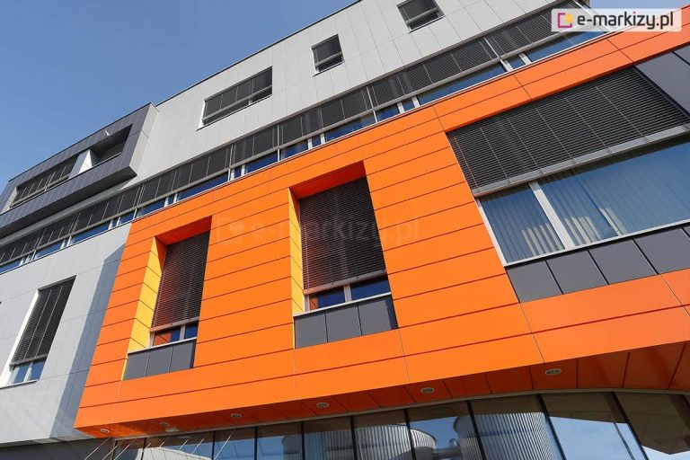 Przykład wykorzystania żaluzji fasadowych podtynkowych do osłony wielu okien w nowoczesnej fasadzie. Ukryte pod warstwą tynku o szarym i pomarańczowym kolorze skrzynki nie zakłócają geometrii elewacji, a jednocześnie chronią pomieszczenia przed nagrzewaniem.