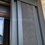 Moskitiera plisowana Top Zag z szarą siatką i antracytową konstrukcją po zwinięciu pakietu zajmuje niewielką przestrzeń we wnęce okiennej.