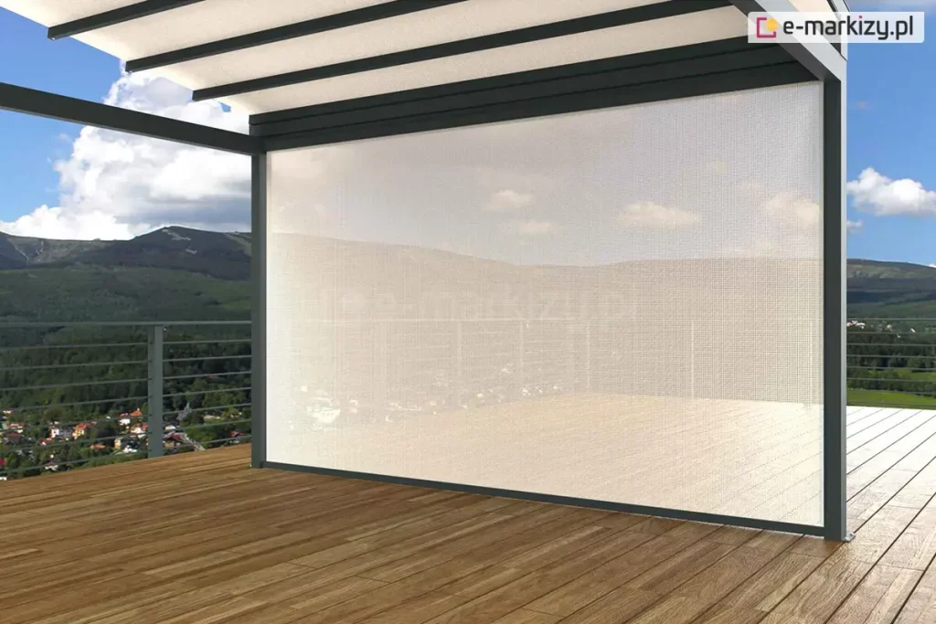 Duże zadaszenie z dachem tkaninowym i ścianką frontową refleksol ZIP z tkaniną przezierną ustawione zostało na drewnianym pustym tarasie. Za metalowymi barierkami w tle widoczne zabudowania, lasy oraz niewysokie góry i niebieskie niebo z kilkoma chmurami.