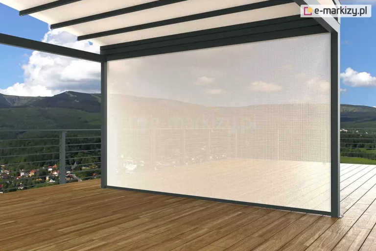 Duże zadaszenie z dachem tkaninowym i ścianką frontową refleksol ZIP z tkaniną przezierną ustawione zostało na drewnianym pustym tarasie. Za metalowymi barierkami w tle widoczne zabudowania, lasy oraz niewysokie góry i niebieskie niebo z kilkoma chmurami.