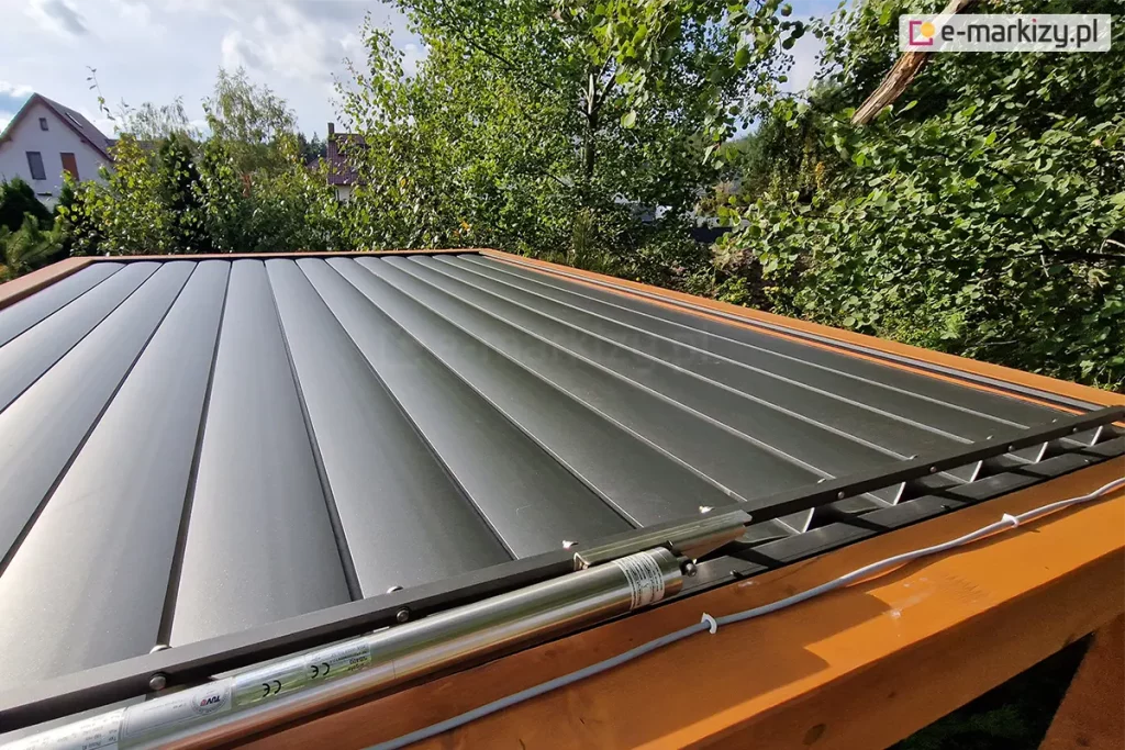 Dach lamelowy SB400 MD z zamkniętymi lamelami w kolorze antracytowym, na pierwszym planie widoczny silnik, kabel zasilający przymocowany do drewnianej belki konstrukcji pergoli oraz mechanizm sterujący ruchem lamel.