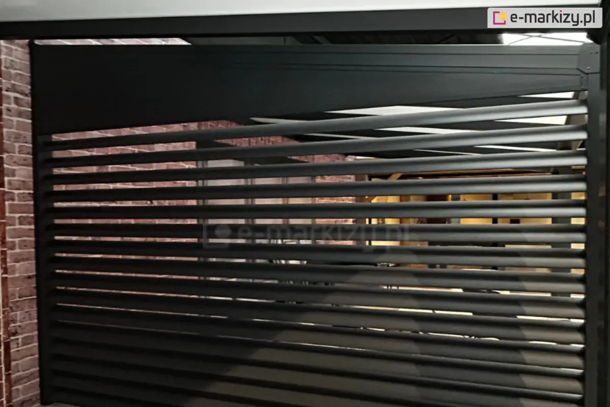 Ścianka żaluzjowa Louvre zamontowana przy pergoli, wykonana z poziomych aluminiowych lameli w kolorze czarnym RAL9005, umieszczona w industrialnym otoczeniu z ceglaną ścianą i nowoczesnym wystrojem wnętrza.