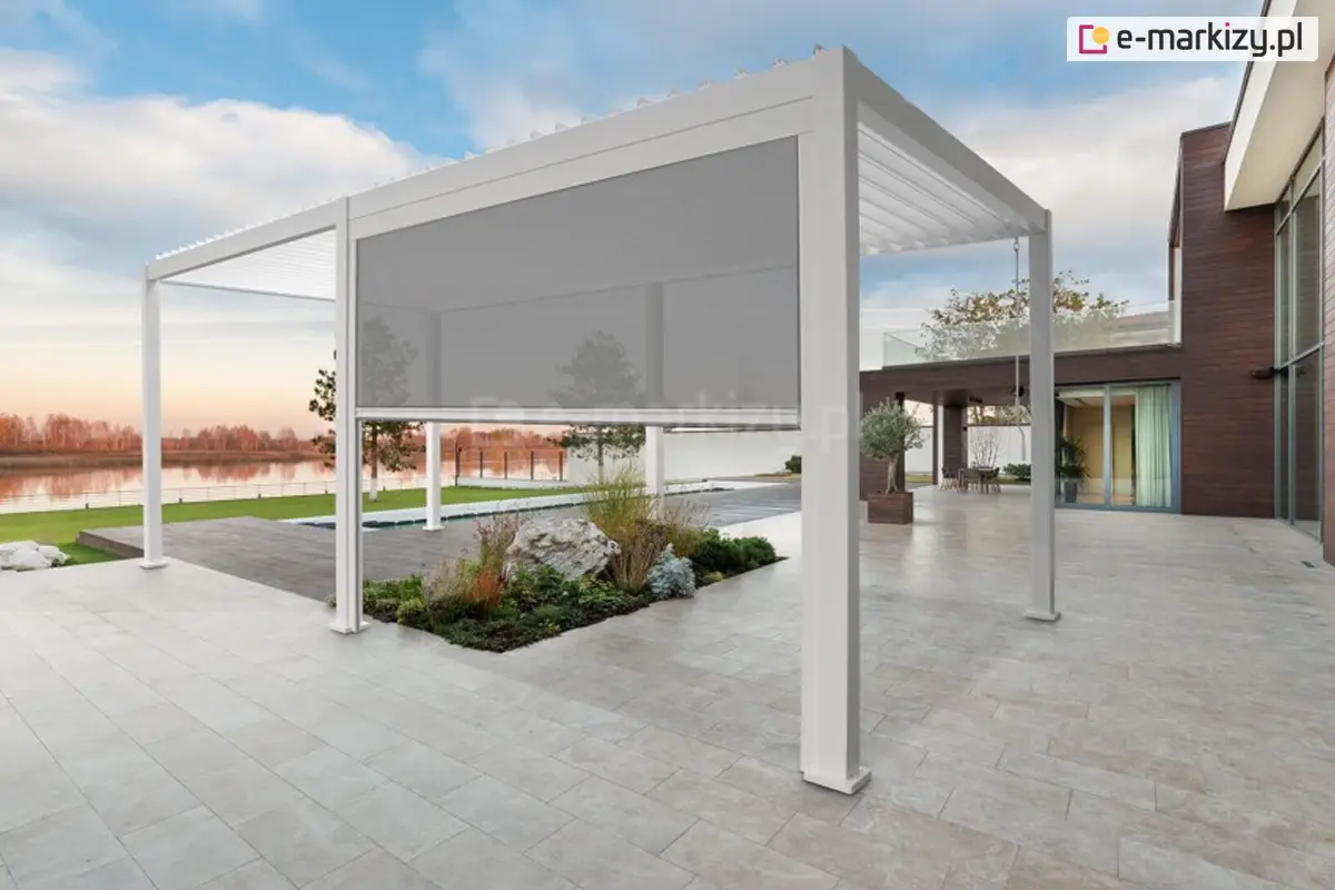 Nowoczesna biała pergola na dużym kamiennym tarasie z opuszczoną szarą roletą screen, widok na basen i jezioro oraz współczesny dom z drewnianą elewacją w tle.
