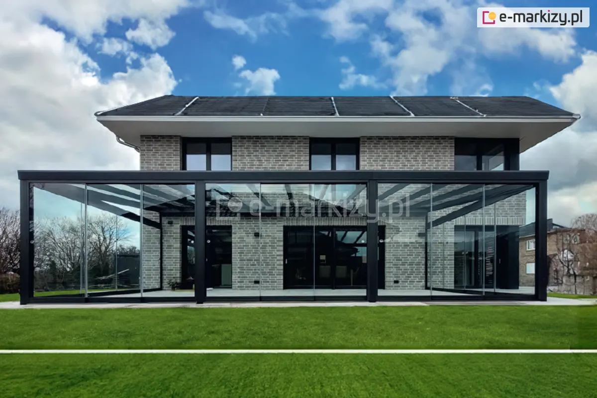 Wielometrowa pergola z czterema frontowymi podporami, wyposażona w trzy zestawy drzwi szklanych Miros między słupami, tworząca elegancką zabudowę tarasową zawierającą ściany przesuwne bezramowe