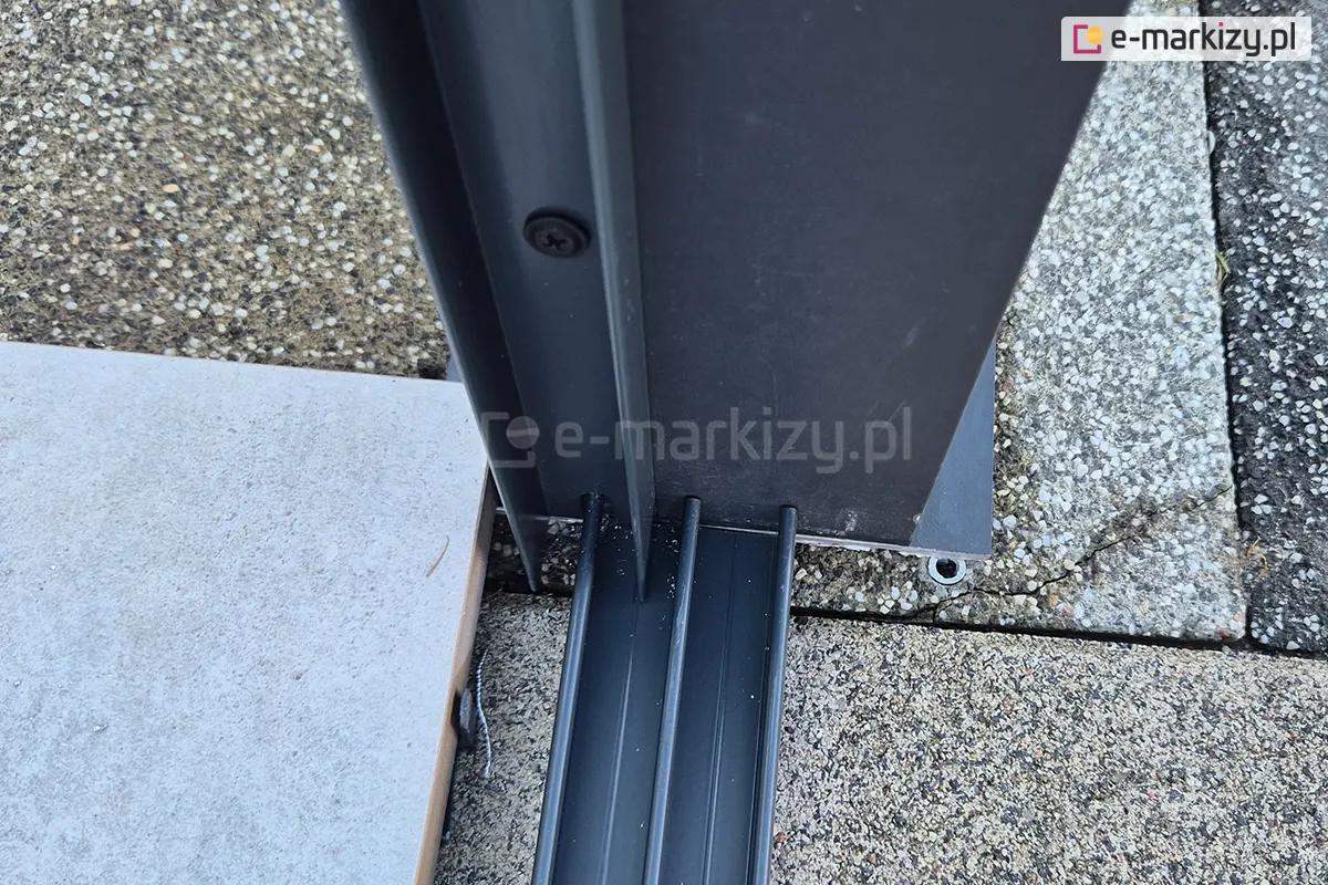 Detal konstrukcyjny ukazujący łączenie prowadnicy dolnej z bocznym profilem aluminiowym systemu drzwi przesuwanych Sotro. Zewnętrzny panel wsuwany jest w profil boczny, co zapewnia lepszą izolację i stabilność zamkniętej osłony.