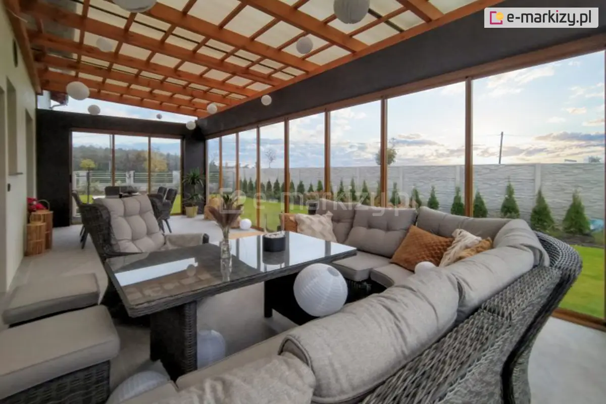 Nowoczesna oranżeria z zestawem wypoczynkowym, przeszklonymi ścianami systemu Sotro i drewnianym osłoniętym dachem – idealna przestrzeń do relaksu przez cały rok.