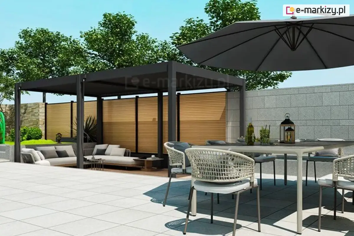Pergola tarasowa Marlo w kolorze antracytowym z dachem z lameli obracanych. Konstrukcja ustawiona przy betonowym murze oporowym, zapewniając prywatność i cień dla wygodnego narożnika wypoczynkowego. Sceneria otoczona zielenią i drzewami, tworząca stylową strefę relaksu na tarasie.