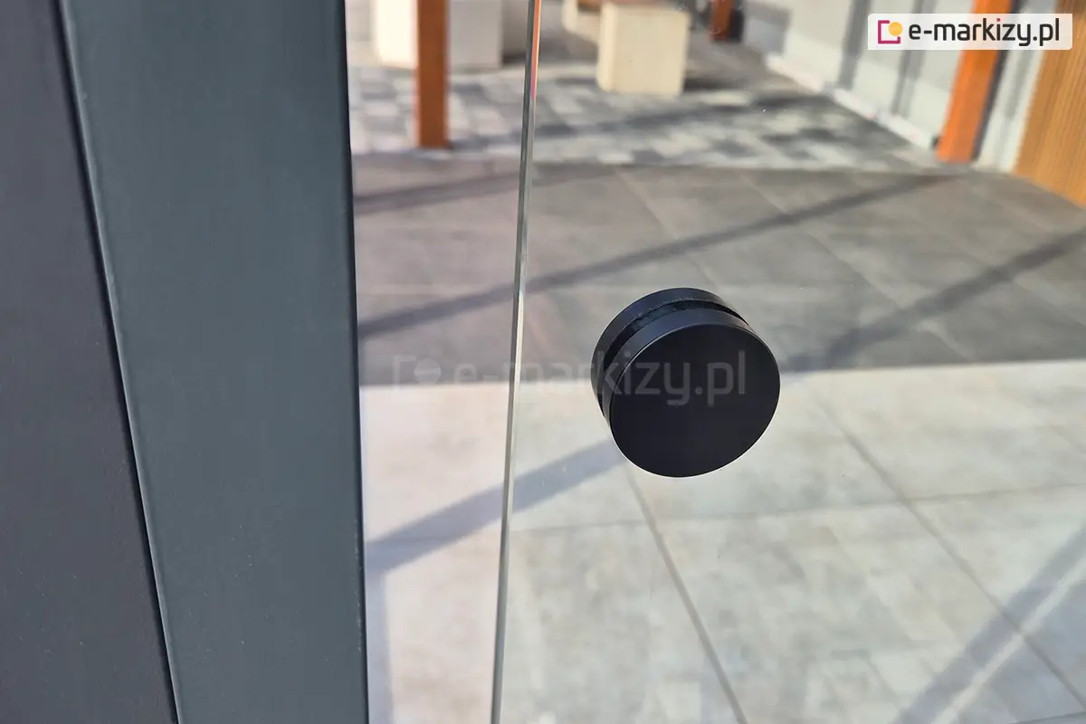 bliżenie na panel szklany systemu Miros z nawierconym, czarnym uchwytem do przesuwania – element nowoczesnej zabudowy tarasu z aluminium wysokiej jakości.