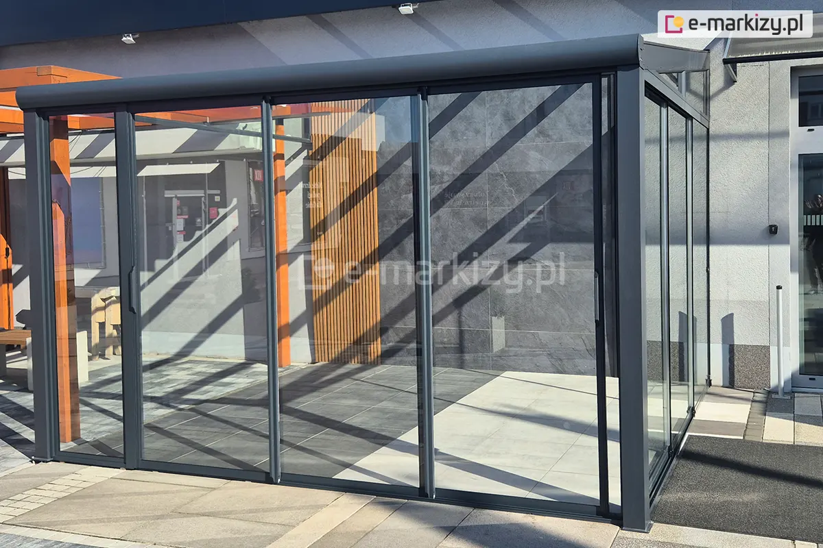 Elegancka pergola szklana wyposażona w nowoczesny system przesuwnych drzwi Sotro z przejrzystym szkłem oraz minimalistycznym charakterem konstrukcji. Jeden z paneli jest w połowie otwarty