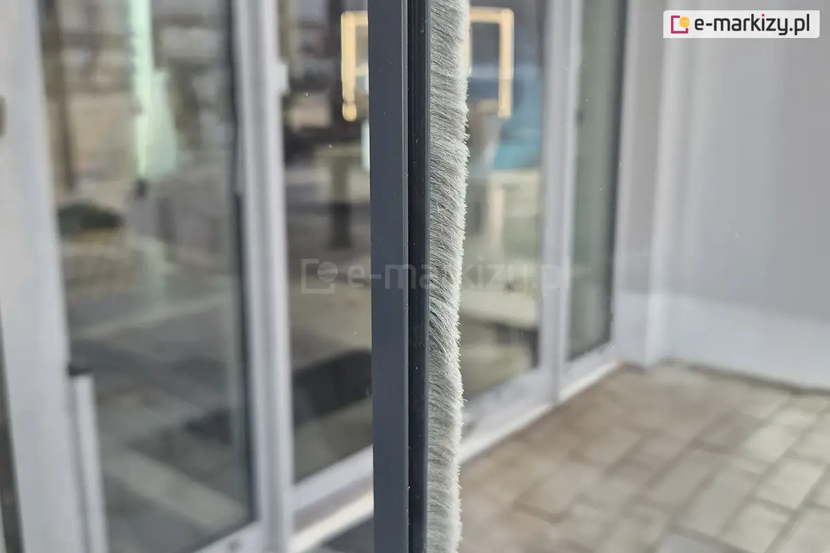 Zbliżenie na przeciwwietrzną listwę szczotkową zamontowaną na przesuwanych drzwiach szklanych systemu Miros, która skutecznie ogranicza przeciągi i poprawia szczelność między panelami zabudowy tarasu.