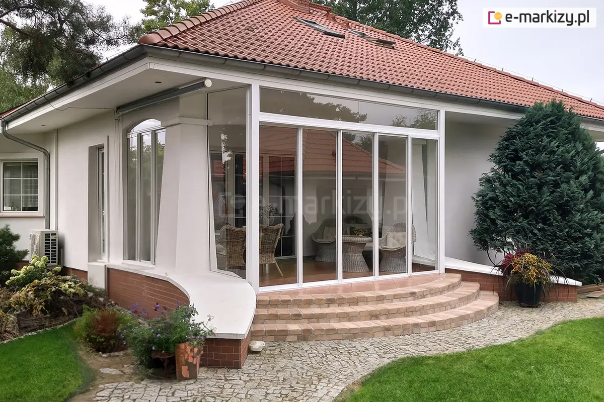 Przesuwane drzwi szklane Sotro zamontowane na werandzie domu jednorodzinnego, prowadzące na zadbany ogród, z lekką białą konstrukcją i przeszklonym wyjściem na taras.