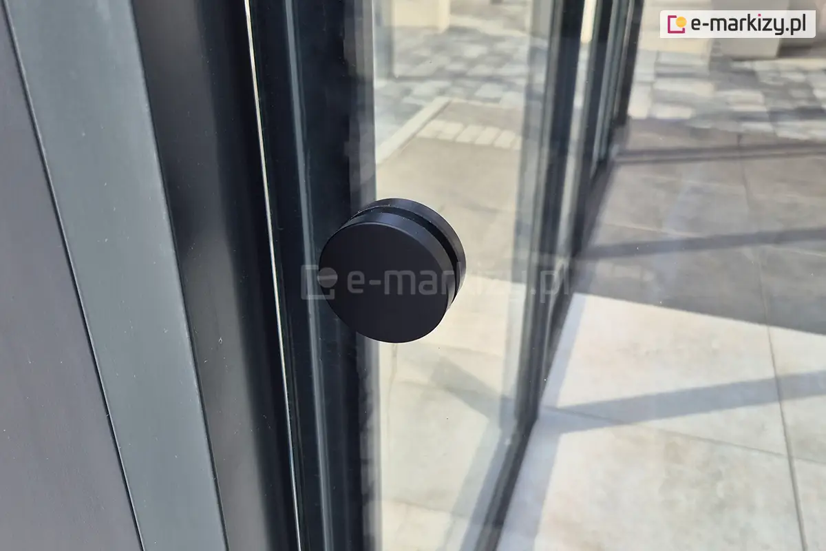 Zbliżenie na czarny, dedykowany uchwyt do przesuwania szyb systemu Miros – szklane panele zamontowane w zabudowie tarasu wykonanej z aluminium wysokiej jakości.