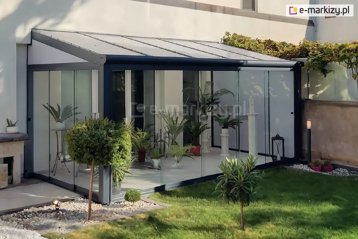 Przesuwne panele szklane Miros na tarasie z dachem poliwęglanowym i bocznymi klinami, tworzące lekką i funkcjonalną zabudowę ogrodową z roślinnością