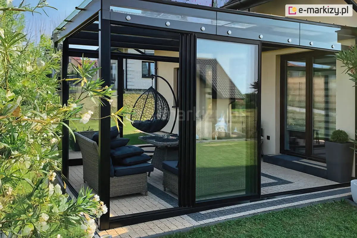 Nowoczesne przesuwne drzwi szklane Sotro z czarną ramą aluminiową zamykające przytulny kącik wypoczynkowy z huśtawką i siedzeniami na tarasie domu jednorodzinnego